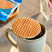A round, individually wrapped vegan and gluten-free maple stroopwafel resting on top of a mug of hot coffee.
