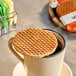 A round vegan speculoos stroopwafel resting on top of a beige mug, with individually wrapped stroopwafels in the background.