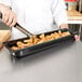 A chef pouring chicken nuggets into a Vollrath black plastic food pan.