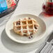 A vegan maple Liege waffle with chocolate chips and powdered sugar on a white plate.