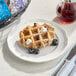 A vegan lemon blueberry Liege waffle served on a white plate with blueberries and a dusting of powdered sugar.