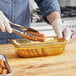 A person in gloves cutting food in a Vollrath amber plastic food pan.