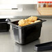 A black Vollrath Super Pan plastic food pan with food in it on a counter.