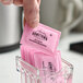 A pink packet of Hometown Provisions zero calorie saccharin sweetener being picked up from a glass container filled with similar packets.