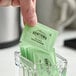 A green packet of Hometown Provisions zero calorie stevia sweetener being picked up from a glass container filled with similar packets.