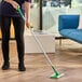 A Swiffer Sweep and Mop floor mopping and sweeping kit with a green and white handle being used to clean a hardwood floor.
