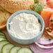 A bowl of whipped cream cheese spread surrounded by bagels, smoked salmon, cucumber slices, red onion, and capers.
