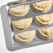 A baking tray with six uncooked short rib flour shell empanadas.