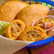 A basket of chicken and potato corn shell empanadas served with a side of salsa and lime wedges.