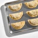 A baking tray with several uncooked flour shell empanadas filled with Cuban pork pernil.