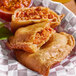 A pizza flour shell empanada filled with a savory meat and tomato mixture, served in a basket with a side of sauce.