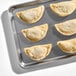 A baking tray with several uncooked flour shell empanadas arranged in rows.
