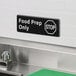 A rectangular black and white sign that reads 'Food Prep Only' with a stop symbol, mounted on a wall above a stainless steel sink.