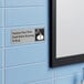 A stainless steel sign that reads 'Employee Must Wash Hands Before Returning To Work' mounted on a light blue tiled wall.