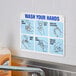 A rectangular white, blue, and black reflective aluminum safety sign displaying handwashing instructions.