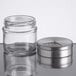 A small clear glass spice shaker with a removable stainless steel adjustable lid.