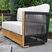 A modern outdoor love seat featuring black rope sides, a teak wood frame, and white Sunbrella cushions.