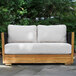 A wooden outdoor love seat with black rope sides and light-colored Sunbrella cushions.