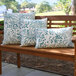 A set of three square and rectangular outdoor pillows with a tropical jade leaf pattern, displayed on a wooden bench.