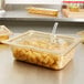 A Vollrath plastic container with food on a salad bar counter with a slotted amber plastic lid.