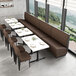 A long brown upholstered single booth with a button-tufted back and walnut finishes, positioned alongside white tables and brown chairs in a modern dining area.
