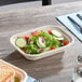 A rectangular compostable fiber container filled with salad, shown on a wooden table.