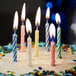 A group of lit multi-colored striped birthday candles on a frosted cake with confetti sprinkles.