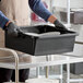 A black heavy-duty polyethylene bus tub or tote box being used to carry dishes in a commercial kitchen setting.