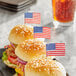 A set of sesame seed hamburger sliders each topped with a small American flag food pick.