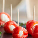 A group of small red peppers stuffed with cheese and skewered with wooden toothpicks.