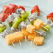 A set of assorted fresh fruit pieces, including strawberries, kiwi, dragon fruit, and cantaloupe, skewered on 6-inch bamboo sticks.