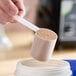 An 80 cc polypropylene scoop with a long handle being used to measure powder from a container.