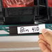 A 1 inch by 3 inch heavy-duty magnetic label or card holder attached to steel shelving, with a handwritten label reading 'Bin 410.'