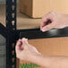 A person applying a black slip strip label holder to the edge of a metal shelving unit.