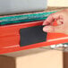 A hand placing a black magnetic label holder onto a red steel shelf.