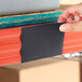 A hand placing a black pre-scored magnetic label holder onto a red steel shelving unit.