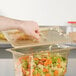 A person's hand using a Vollrath amber high heat slotted lid to cover a container of vegetables.