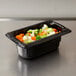 A black Vollrath plastic food pan with vegetables in it on a counter.