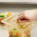 A person's hand pushing a Vollrath Super Pan high heat plastic lid onto a container of food.