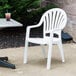 A white Grosfillex Pacific Fanback stacking chair on a concrete patio.