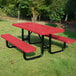A red perforated metal picnic table with attached benches and black metal legs, situated outdoors on grass.