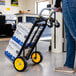 A steel convertible hand truck with yellow wheels being used to transport boxes in an office setting.
