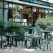 A green plastic Grosfillex Miami bistro chair on a brick surface next to a green table.