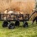 A steel utility cart loaded with firewood being pulled across grass.