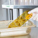 A hand in white gloves holding a yellow plastic Vollrath high heat drain tray in a metal container.