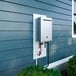 A wall-mounted outdoor tankless water heater with recirculation pump installed on the exterior of a house.