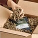 A box filled with brown crinkle paper shred being used as packing material around a bag of organic coffee.