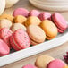 A tray of assorted colorful macarons in pink, yellow, and beige, some with sprinkles.