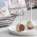 A pair of individually wrapped cookies and cream cake pops coated in white chocolate, displayed on a white plate.
