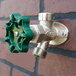 A wall-mounted non-freeze anti-siphon hydrant with a green handle attached to a brick wall.
